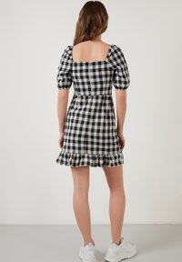 Rutig klänning i marinblått och krämfärgat, med fyrkantig halsringning, puffärmar, figursydd midja och volangnederdel. Bärs med vita sneakers.