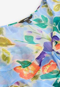 Genomskinlig blommig blus i mjuk blå färg, med färgglada blommor i orange, rosa, lila och grön. Rynkad design med en lätt textur.