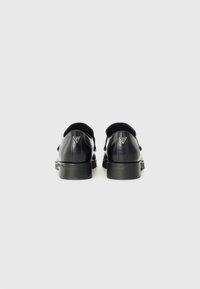 Des chaussures en cuir noir avec une finition lisse, un bout arrondi et un petit talon. Détail du logo en forme de triangle argenté sur le talon.
