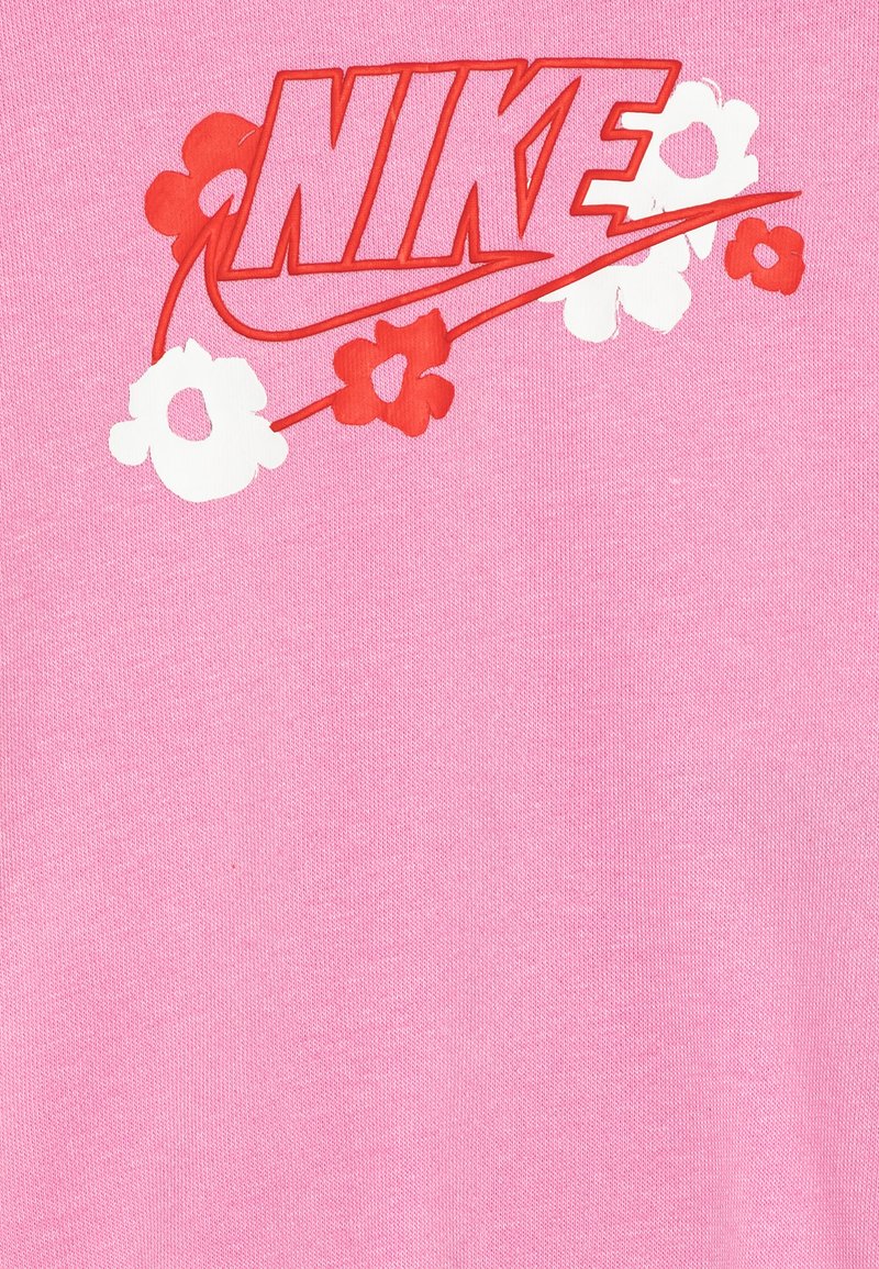 T-shirt in cotone rosa con un audace logo "NIKE" rosso circondato da grafiche floreali rosse e bianche. Texture liscia, maniche corte.