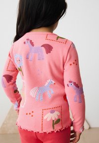 T-shirt à manches longues rose rayé avec des motifs colorés de licornes et de fleurs, doté d'un ourlet ondulé et d'un tissu texturé. Les accents incluent des motifs à pois.