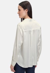 Weiße Bluse mit langen Ärmeln und Kragen, aus weichem Stoff, lässiger Schnitt und Rückenteilen mit Falten. Mit Knopfmanschetten und glatter Textur.