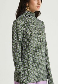 Haut à col roulé à manches longues en vert, présentant un motif géométrique en violet et blanc. Tissu doux avec une silhouette ajustée.
