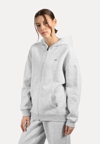 Szara bluza zip-up wykonana z miękkiej mieszanki bawełny, z przestronnym kapturem, przednimi kieszeniami i ściągaczami. Minimalistyczny design z logo.