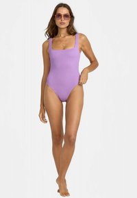Maillot de bain une pièce violet à côtes avec encolure carrée. Modèle portant des lunettes de soleil oversize, design minimaliste, texture lisse, coupe ajustée.
