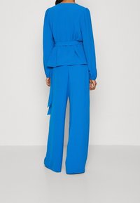 Blue two-piece outfit featuring a peplum top with long sleeves and wide-leg trousers, made from textured fabric. Belts at waist.