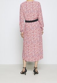 Abito lungo aderente in stampa animalier rosa e rossa con maniche lunghe. Una cintura nera definisce la vita. Indossato con scarpe nere con tacco.