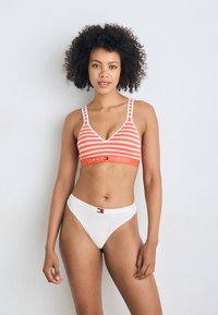 Rood-wit gestreepte bralette met een v-hals en dikke banden, gecombineerd met witte hooggetailleerde slipjes. Beschikt over logo-accenten. Gladde textuur.