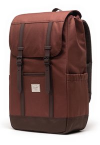 Mochila de lona marrón con correas ajustables, tapa superior y acentos de cuero marrón. Cuenta con un bolsillo frontal y una espalda de malla transpirable.