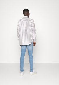Camisa de manga larga a rayas en beige claro y blanco, combinada con jeans ajustados azul claro y zapatillas blancas, vista desde atrás.