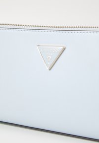 Světlomodrá peněženka z umělé kůže se stříbrnými kovovými doplňky, s trojúhelníkovým raženým logem a zipovým uzávěrem podél horního okraje.