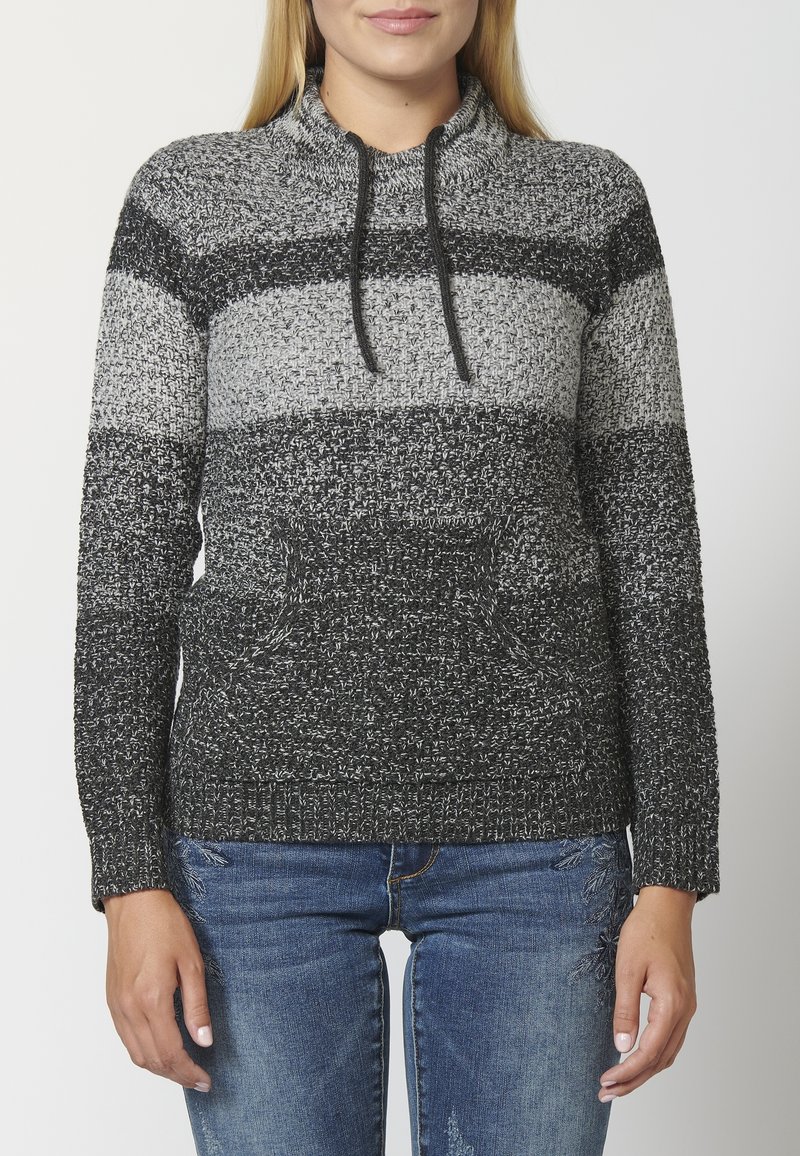 Grijs en zwart gestreepte gebreide trui met een hoge hals, koordjes en een voorzak, gecombineerd met blauwe versleten jeans.