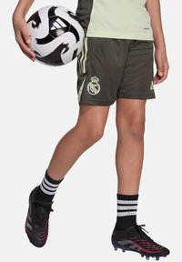 Zwart-witte voetbalsbal met een patroont ontwerp, gedragen met olijfgroene shorts met een logo, zwarte voetbalschoenen en gestreepte zwarte sokken.