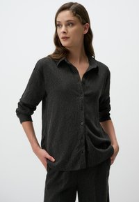 Zwarte textuur knoopshirt met een kraag en lange mouwen opgerold bij de manchetten, met verticale strepen en een relaxte pasvorm.