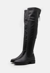 Botas negras por encima de la rodilla, hechas de material suave, con puntera redonda, tacón bajo y detalle de cremallera lateral para facilitar su uso.