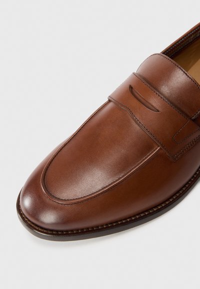 Mocasín de cuero marrón con acabado suave,puntera redondeada y detalle decorativo de cortes en el empeine. Suela cosida y diseño minimalista.