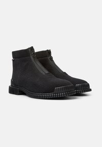 Svarta ankelskor med ribbat tyg och dubbla dragkedjor. Gummisulor med distinkt räfflad textur. Slip-on design för enkel användning.