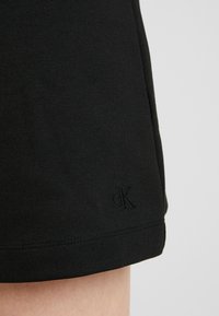 Gonna nera in cotone con una sottile texture e orlo cucito, con un logo "CK" ricamato nell'angolo in basso a sinistra.