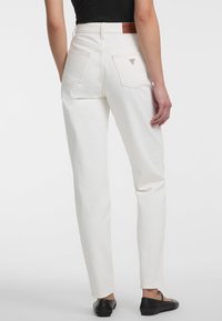 Pantalones de denim blanco con cintura alta y corte ajustado. Presentan bolsillos traseros y una etiqueta de cuero en la cinturilla. Llevados con unos zapatos planos negros.