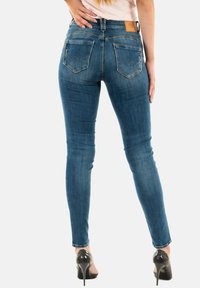 Dunne blauwe spijkerbroeken van denim met een gladde textuur, middelmatige wassing, gestikte achterzakken met een gebogen ontwerp en een leren label op de tailleband.