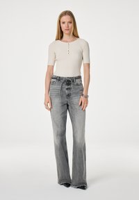 Geribbelde crèmekleurige top met korte mouwen en knopen; gecombineerd met hooggewaardeerde vervaagde grijze flared jeans met rafelige zoom.