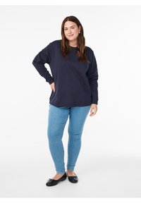 Tumesinist värvi pikkade varrukatega pusa lõdva lõikega, soonikkoega kraega, millele on lisatud helesinised kitsad teksapüksid ja mustad baleriinikingad.