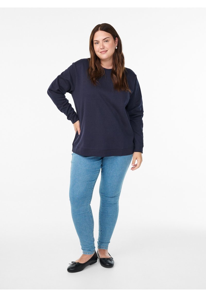 Tumesinist värvi pikkade varrukatega pusa lõdva lõikega, soonikkoega kraega, millele on lisatud helesinised kitsad teksapüksid ja mustad baleriinikingad.