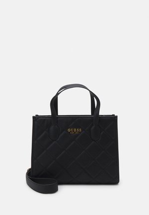 Czarna pikowana torebka z podwójnymi uchwytami u góry, odpinanym paskiem na ramię oraz złotym logiem "GUESS EST 1981" z przodu.