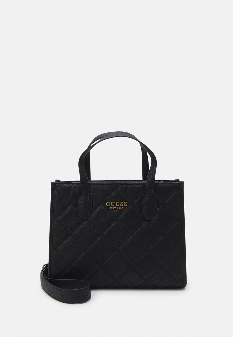 Sac à main noir matelassé avec double anses supérieures, une bandoulière amovible et un logo doré « GUESS EST 1981 » à l’avant.