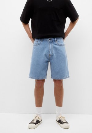 Lichtblauwe denim shorts met een relaxte pasvorm, voorzien van voorzakken en riemlussen, gecombineerd met een zwart shirt met korte mouwen en sneakers.