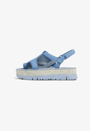 Blå plattformssandaler med flera remmar, tillverkade av ett mjukt material. Sulan är ljusgrå med prickig textur och en tjock, vadderad bas.