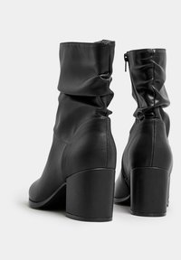 Mustat nahkasaappaat nilkkapituisella, rypistyneellä varrella, pyöreällä kärjellä ja paksuilla kengänpohjilla. Vetoketjukiinnitys sisäpuolella. Tasainen pinta ja vähäinen yksityiskohtaisuus.