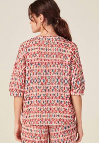 Blusa de manga corta en tejido ligero, con un patrón abstracto colorido en rojo, azul y crema. Con dobladillo recto y corte holgado.