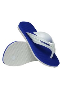 Chancla de goma azul con una plantilla texturizada, tira blanca y detalle del logo. La suela blanca presenta un ribeteado horizontal para mayor agarre.