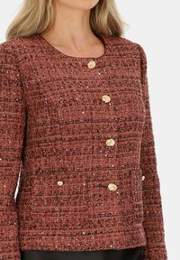 Rdzawokolorowy żakiet z tweedu o fakturowanym wzorze, z złotymi guzikami w kształcie róży, okrągłym dekoltem oraz podwójnymi kieszeniami z przodu.