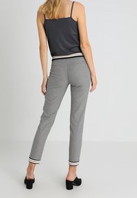 Grå linne med tunna axelremmar parat med svart-vita rutig byxor med tapered passform och randiga vristhöljen. Klackskor i svart.