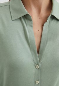 Light green collared shirt made of soft fabric, featuring a button placket with two buttons and a relaxed fit.