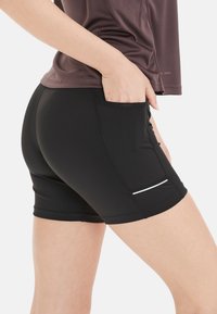 Zwarte sportshorts met een strakke pasvorm, gemaakt van rekbaar materiaal, voorzien van een zijzak en een reflecterende witte accent.