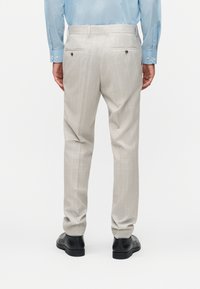 Άνδρας που φαίνεται από πίσω, φορώντας μπεζ παντελόνι με ρίγες, μαύρα παπούτσια επίσημου τύπου και ανοιχτό μπλε πουκάμισο με μακριά μανίκια, μπατισμένο μέσα στο παντελόνι.