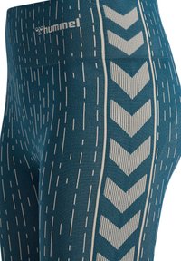 Legginsy w kolorze morskim z pionowym wzorem kropek, białe paski w jodełkę z boku oraz logo „hummel” na górnej części uda.