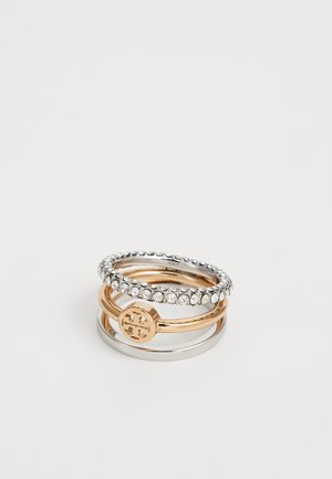 Stack of three rings: one gold with cutout design, one gold smooth band, and one silver band with clear rhinestones.
