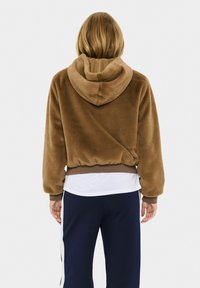 Hnědá zkrácená mikina s měkkou, chlupatou texturou, která má kapuci se stahovací šňůrkou a elastický pas, v kombinaci s námořnickými kalhotami.