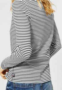Top s dlouhým rukávem v černobílých vodorovných pruzích, bavlněný materiál, žebrovaná textura, s malou obdélníkovou značkou značky na lemu.