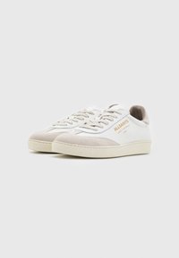 Sneaker bianche con dettagli in suede beige, punta tonda, suola piatta in gomma e decorazione dorata con il marchio. Lacci e linguetta imbottita.