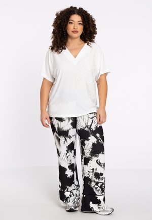 White, short-sleeve blouse with a V-neck and butterfly outline design; paired with black and white tie-dye patterned wide-leg pants.