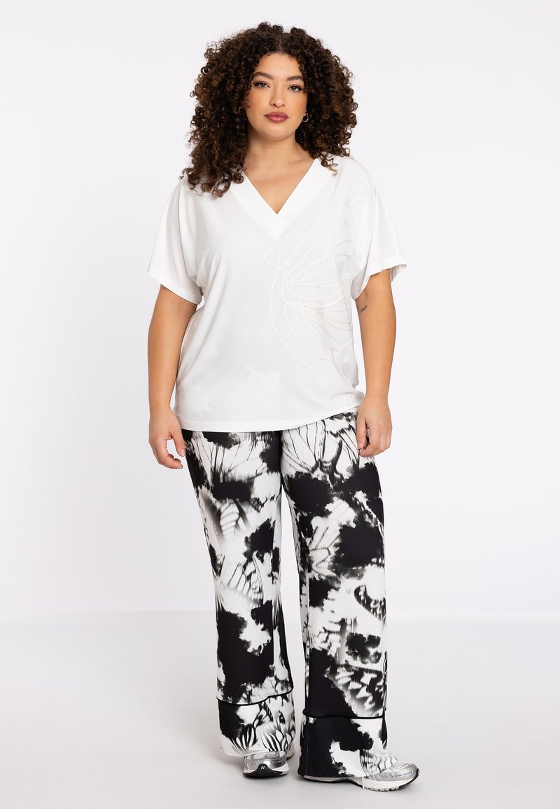 Witte blouse met korte mouwen en een V-hals, versierd met een vlinderomtrek; gecombineerd met zwart-witte tie-dye wijde broek.