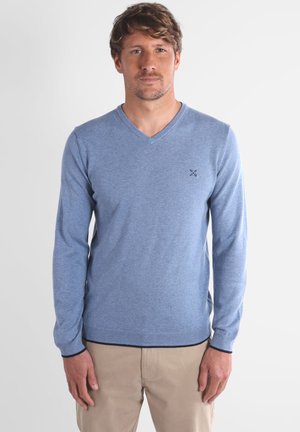 Pull-over bleu clair à manches longues et décolleté en V, fabriqué dans un tissu doux. Il présente un petit logo sur la poitrine ainsi que des poignets et un ourlet côtelés.