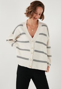Cárdigan crema con rayas en espiga negras, escote en V profundo y cierre de seis botones. Material de punto suave con mangas largas.