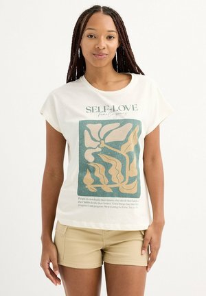 Camiseta de algodón color crema con un corte relajado, que presenta un gráfico abstracto en tonos azul verdoso y beige, junto con un texto motivacional en la parte frontal.