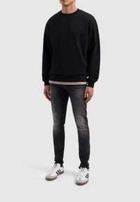 Zwarte sweatshirt met een ronde hals, ribgebreide manchetten en zoom. Draag het over een beige shirt, in combinatie met donkere jeans en witte sneakers.